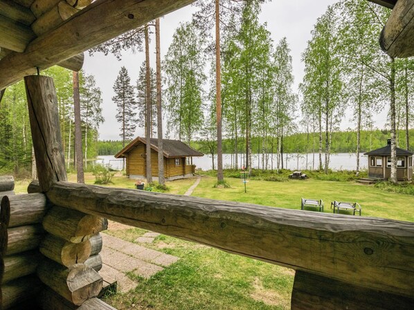 Une cabane dotée d’une terrasse en bois donnant sur un lac, entourée de grands arbres.