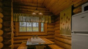 A log cabin interior with a wooden table and benches, a window with curtains, a refrigerator, and a painting on the wall. - Aurinkoniemi by Interhome (Hankasalmi)
