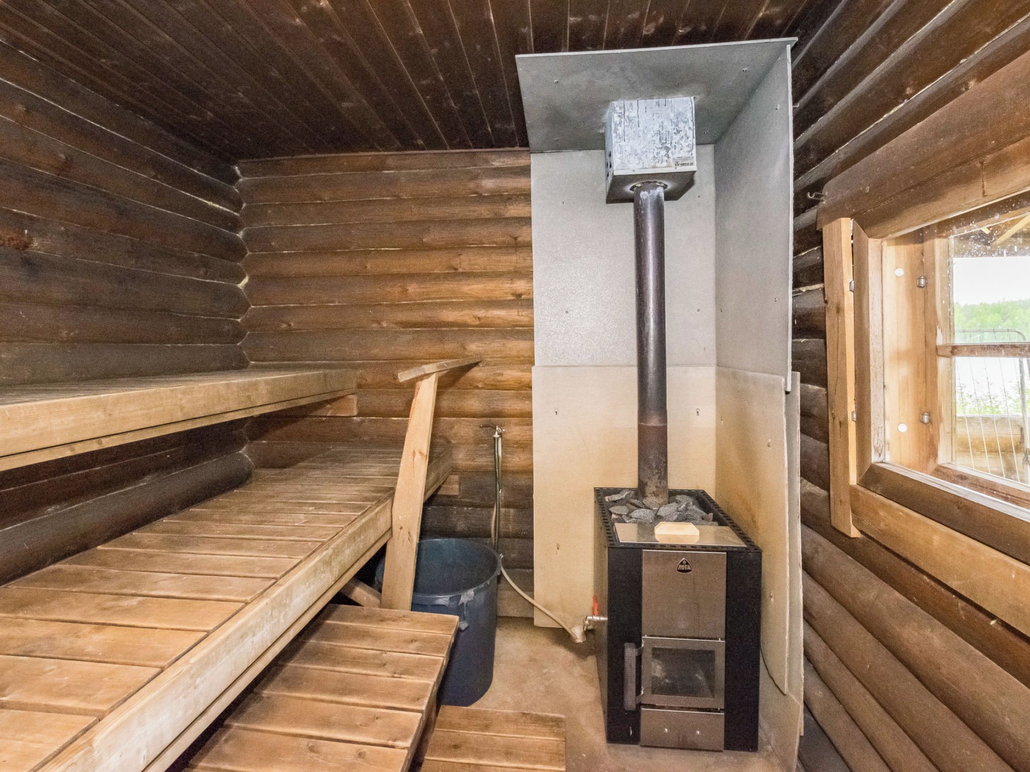 A wooden cabin interior with a wood stove, a window, and a door.