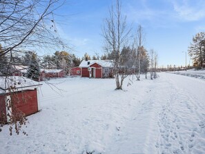 Et snedækket landskab med et rødt ladehus og flere mindre bygninger, en klar himmel og en vej med vejskilte.