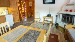 A cozy cabin interior with a wooden interior, a television mounted on the wall, a fireplace, and a kitchen area with a coffee maker and a dishwasher.