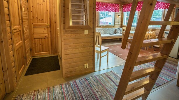 A wooden interior with a staircase, a sofa, and a window with floral curtains.