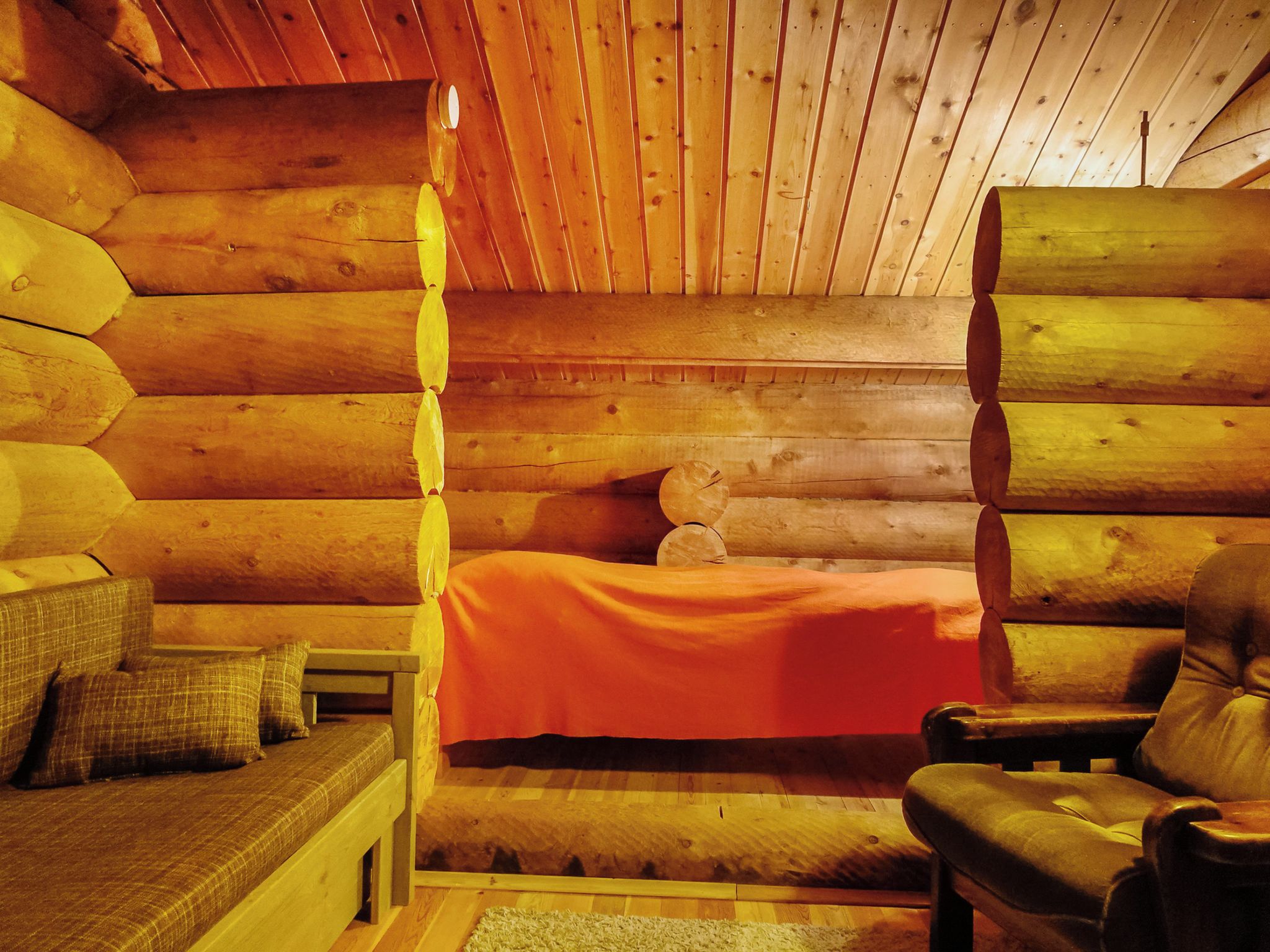 A log cabin interior with a bed, a chair, and a sofa.