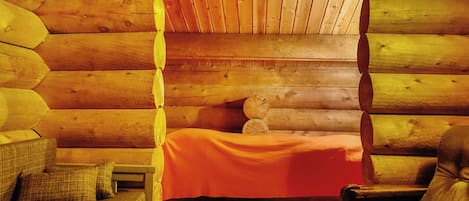 Interior de uma cabana de madeira com uma cama, uma poltrona e um sofá.