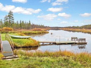 A calm lake with a dock, a small boat, and a wooden pier with benches.