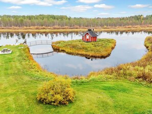 A lakeside property with a small red cabin, a wooden dock, and a grassy area.