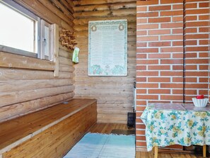 A wooden cabin interior with a bench, a table with a floral tablecloth, and a bulletin board with text.