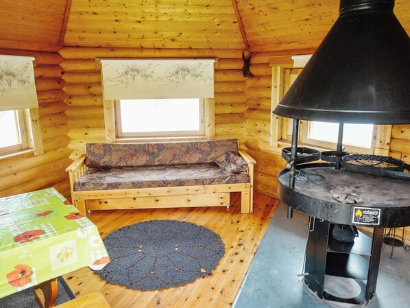 A cozy cabin interior with a wooden sofa, a table with a floral tablecloth, and a wood-burning stove.