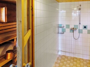 A bathroom with white tiled walls, a shower area, and a wooden bench.