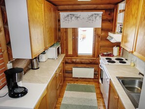 A compact kitchen with wooden cabinets, a stove, a sink, and a window with a view of the outside.