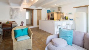 A modern kitchen with a central island, a dining area with a wicker chair, and a living room with a sofa. - Vacation home Hoche by Interhome (Quiberon)