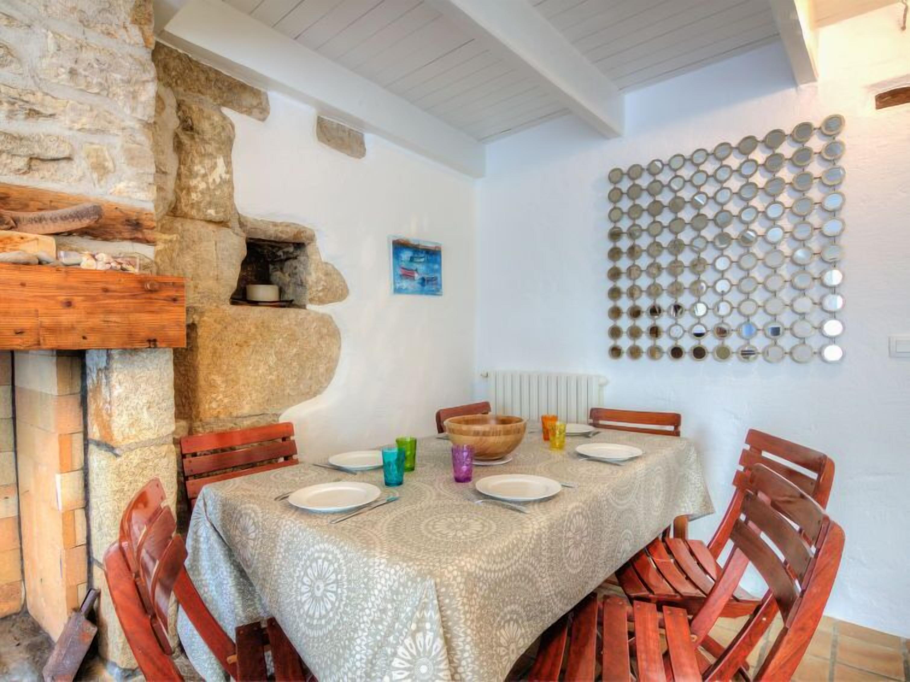 Un coin repas agrémenté d’un mur en pierre, de chaises en bois, d’une table recouverte d’une nappe à motifs et d’une décoration murale composée de miroirs ronds.