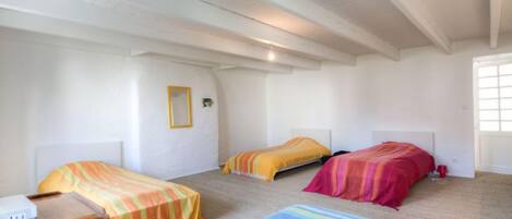 Een kamer met drie bedden, elk met een ander kleurend beddegoed. Er staat een houten nachtkastje met een apparaat erop, en een raam aan de rechterkant.