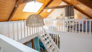 An attic bedroom with a sloped wooden ceiling, a white railing, and a hanging light fixture. - Vacation home Hoche by Interhome (Quiberon)