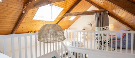 An attic bedroom with a sloped wooden ceiling, a white railing, and a hanging light fixture.