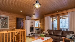 Ein gemütliches Blockhaus-Interieur mit Holzvertäfelung, Kamin, einer Couch und einem Essbereich.