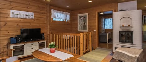 A cozy cabin interior with a wooden dining table, a sofa, a television, and a fireplace.