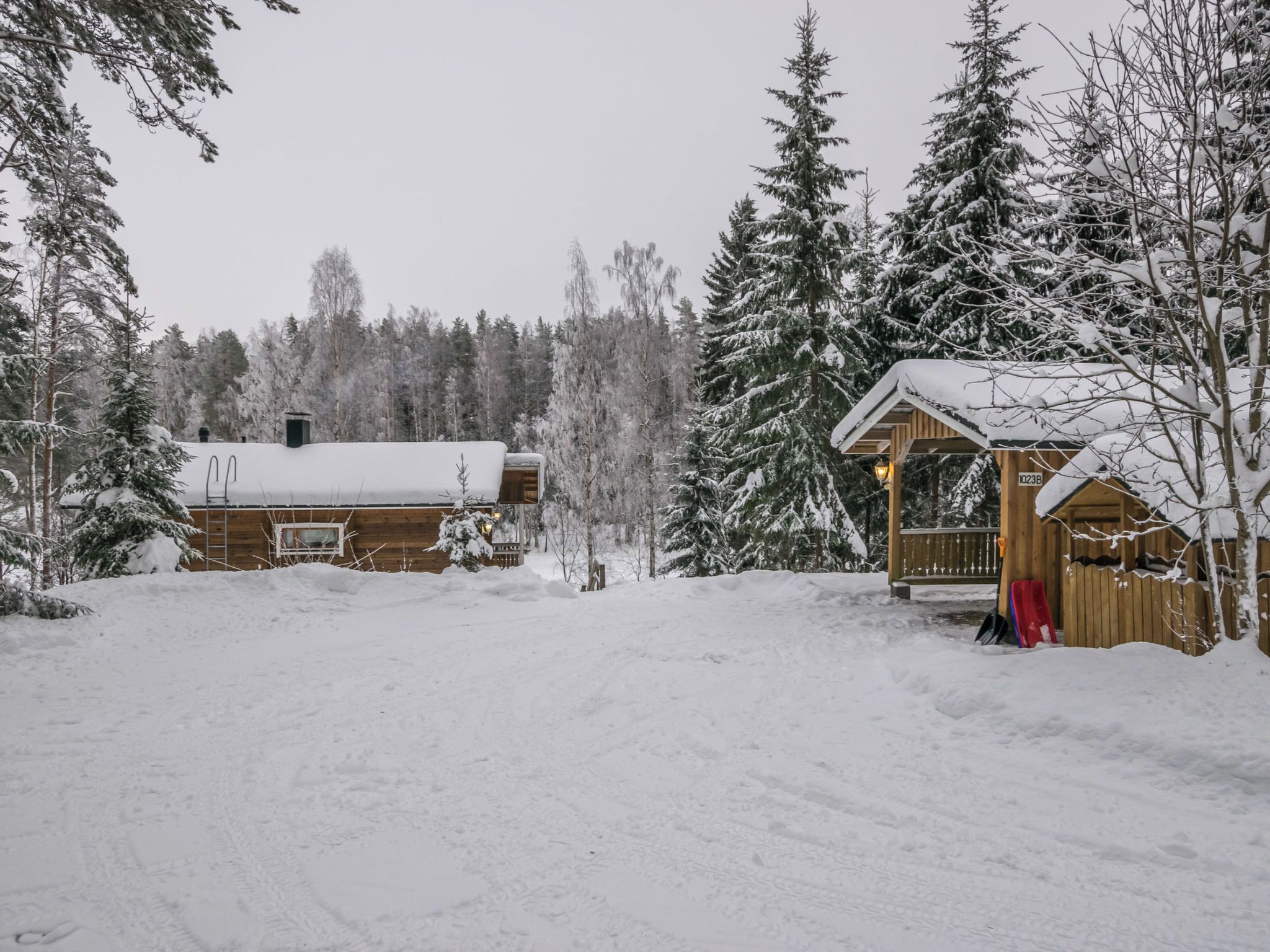A wooden cabin with a snow-covered roof, surrounded by evergreen trees.