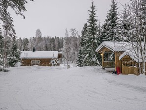 Una cabaña de madera con techo nevado, rodeada de árboles de hoja perenne.