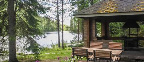 A gazebo with a hexagonal roof overlooking a lake, surrounded by a garden with benches and flowers.