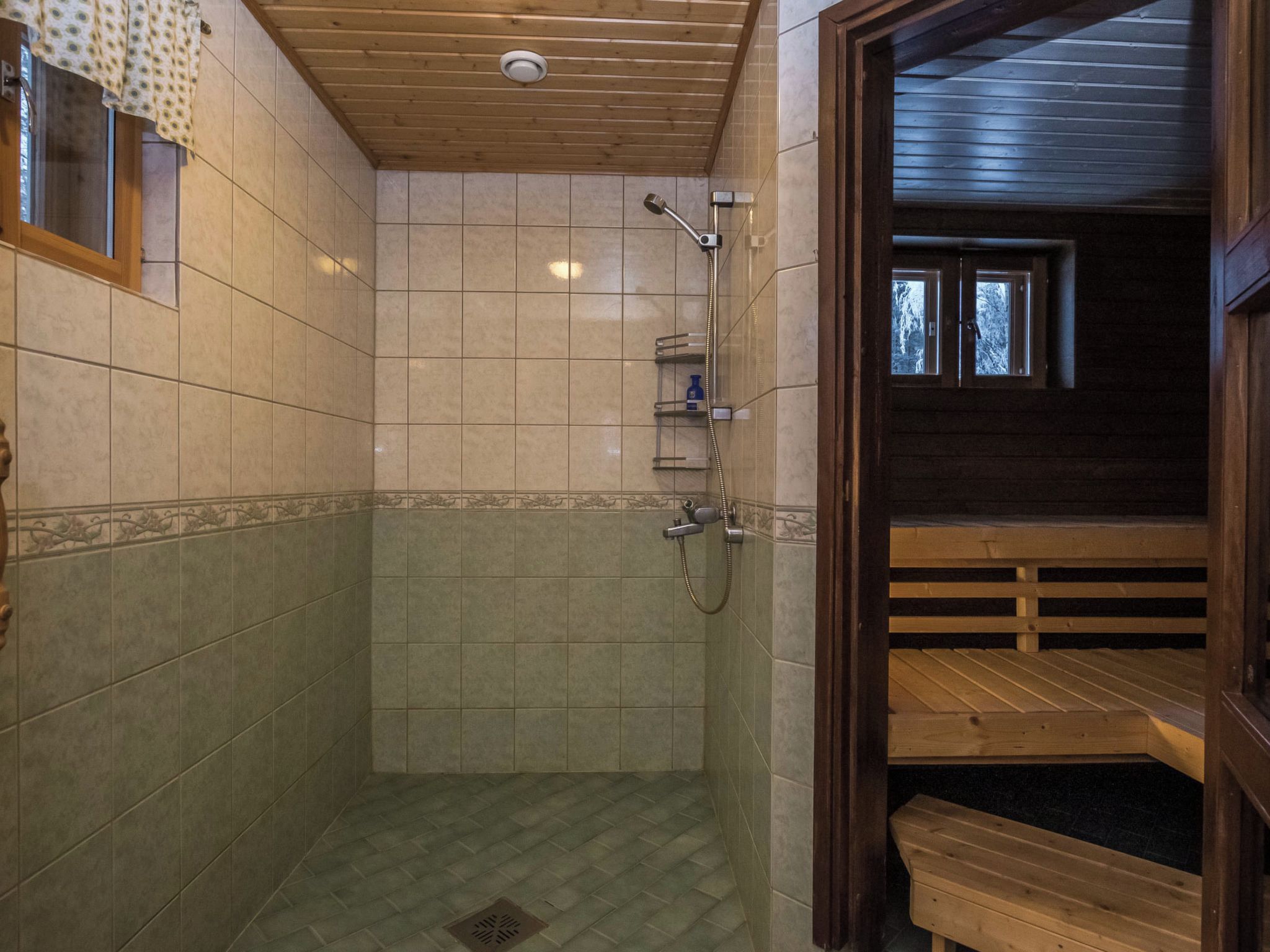 Een douchegedeelte met betegelde wanden, een houten plafond, en een bankje in de aangrenzende kamer.