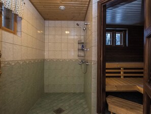 Un área de ducha con paredes de azulejos, techo de madera, y un banco en la habitación contigua.