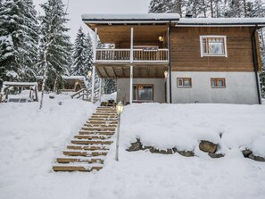 Een houten hutje met een houten trap naar een balkon, omgeven door met sneeuw bedekte bomen.