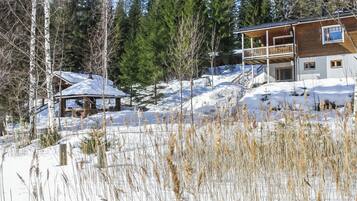 Una cabaña de madera con balcón, rodeada de nieve y árboles.