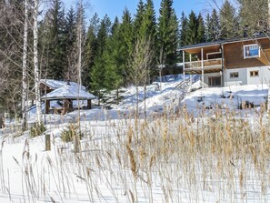 A wooden cabin with a balcony, surrounded by snow-covered ground and trees.