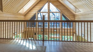 Um quarto espaçoso no sótão, com vigas de madeira, janelas amplas e vista para o exterior.