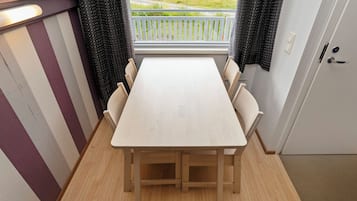 Een eetgedeelte met een houten tafel en stoelen, een raam met gordijnen en uitzicht op een grasveld.