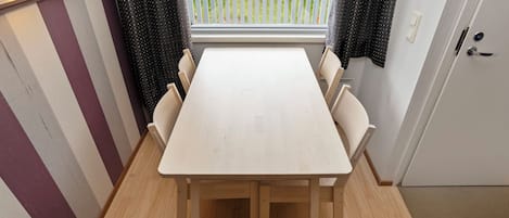 Ein Essbereich mit einem Holztisch und Stühlen, einem Fenster mit Vorhängen und Blick auf eine Rasenfläche.
