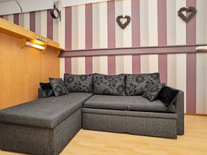 A sectional sofa with floral upholstery, a wooden shelf with a light fixture, and a striped wall with heart-shaped decorations.