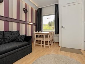 Una habitación con una pared a rayas, un sofá con cojines estampados, una mesa de madera con sillas, una ventana con cortinas y una puerta.