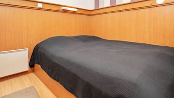 Een kamer met een enkel bed, houten lambrisering, een radiator en een gestreepte wand.