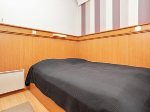 Ein Zimmer mit einem Einzelbett, Holzwandverkleidung, einem Heizkörper und einer gestreiften Wand.