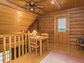 A wooden cabin interior with a dining table, chairs, a ceiling fan, and a window with a view.