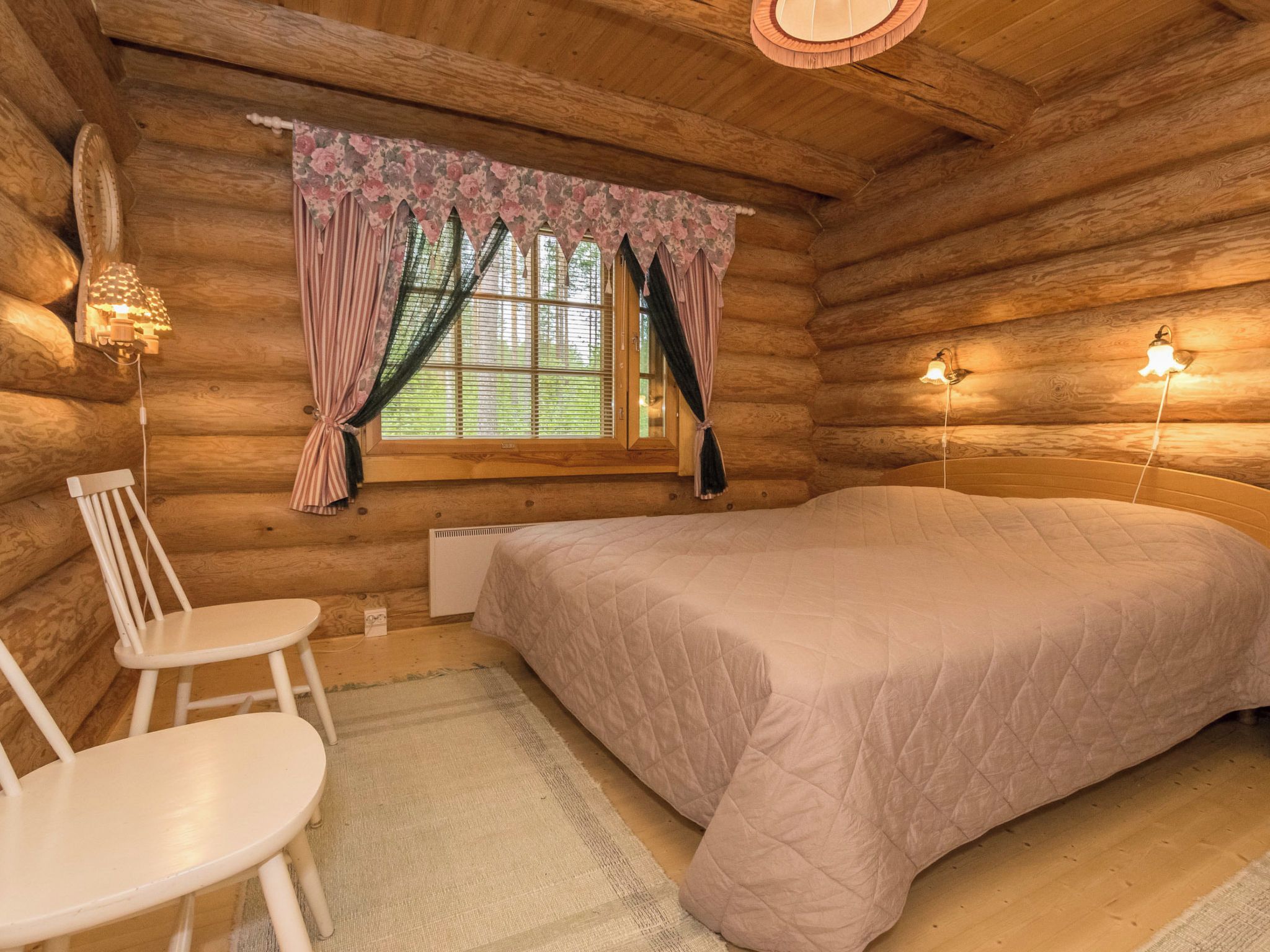 Un dormitorio tipo cabaña de madera con una cama, una silla, una mesa y una ventana con cortinas.