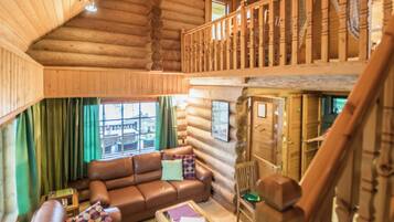 Interno di una baita in legno con una scala in legno, un divano in pelle e vista dalla finestra.