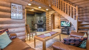 Interior acogedor de una cabaña de troncos con chimenea de piedra, sofás de cuero, una mesa de centro de madera y una escalera de madera.