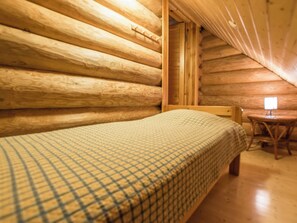 A single bed with a checkered bedspread in a log cabin room with wooden walls and a sloped ceiling.
