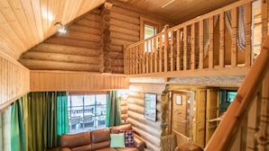 Interior de una cabaña de troncos con un dormitorio en el altillo, una sala de estar con un sofá de cuero marrón y un comedor.