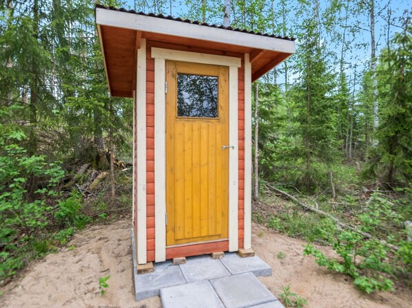 A small wooden cabin with a yellow door, surrounded by dense forest.