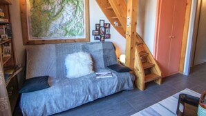 Ein gemütliches Wohnzimmer mit einer Holztreppe, einem Sofa mit weißem Kissen, einer gerahmten Karte an der Wand und einer rosafarbenen Tür.