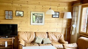 Ett mysigt vardagsrum med en väggpanel av trä, en soffa i läder, ett soffbord, en tv och inramade tavlor.