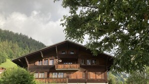 En traditionell chalet i trä med flera balkonger, belägen i ett bergigt område med frodig grönska.