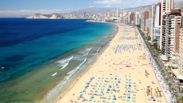 A coastal cityscape with a wide sandy beach lined with tall buildings, a clear blue sea, and a mountainous backdrop. - La Goleta by Interhome (Benidorm)