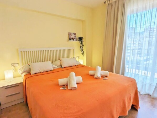 A hotel room with a bed, a nightstand, a wall-mounted photo, and a window with curtains.