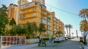 A multi-story residential building with balconies, parked cars, and palm trees. - La Goleta by Interhome (Benidorm)