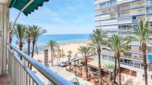 A balcony with a view of a beach, palm trees, and a multi-story building with balconies. - La Goleta by Interhome (Benidorm)